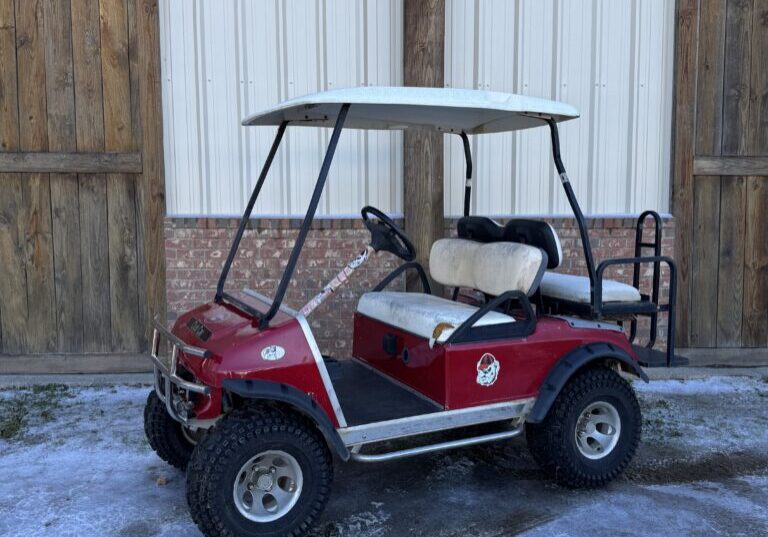 Red golf cart parked outside on snowy ground near wooden doors.