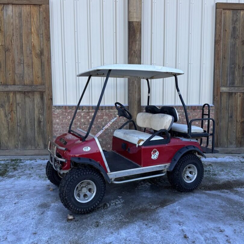 Red golf cart parked outside on snowy ground near wooden doors.