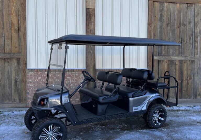 Black golf cart with roof parked on snowy ground outside a building.