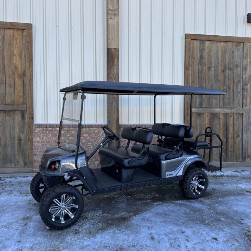 Black golf cart with roof parked on snowy ground outside a building.