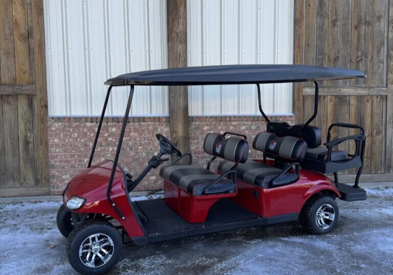 Red six-seater golf cart parked on snowy ground near a building.