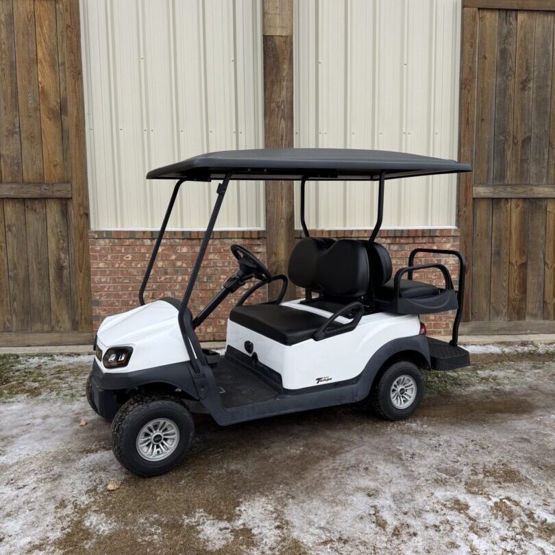 White golf cart parked on a snowy driveway beside a wooden fence.