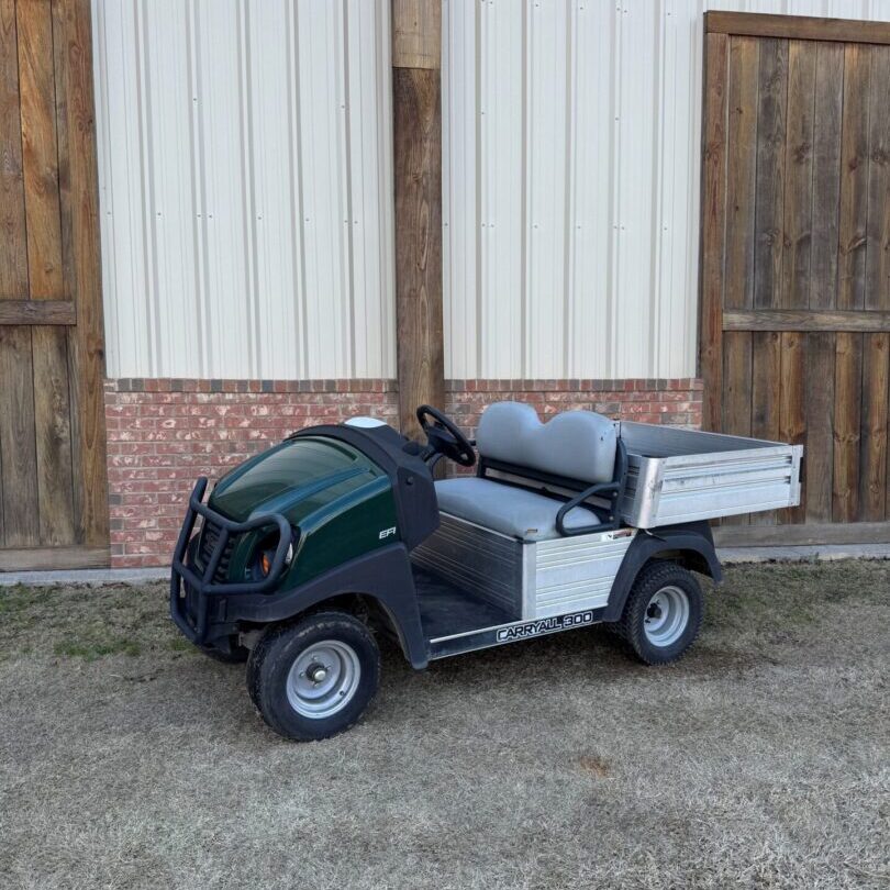 A compact green utility vehicle parked outside wooden doors.